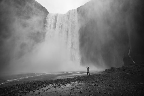 Iceland Travel Photography Tourist taking a photo in the spray at Skogafoss Waterfall Skogar South Region Sudurland Iceland