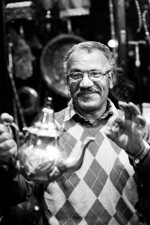 Morocco Travel Portrait Photography Black and white photo of a Moroccan teapot market vendor in Marrakech souk and market Morocco North Africa