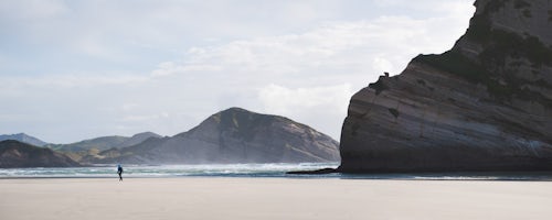 New Zealand Travel Photography Panoramic Photo of a Backpacker Walking Along Deserted Windy Wharariki Beach Golden Bay South Island New Zealand